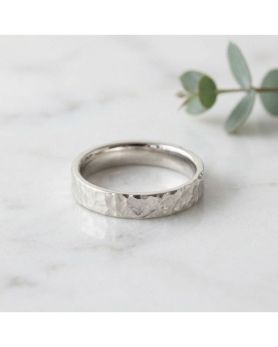Alliance effet martelé pour femme en or - bague argentée à texture martelée sur fond clair, avec plante en arrière-plan.