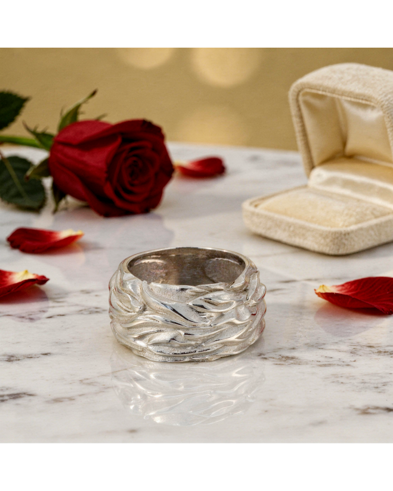 Alliance FLAMME pour femme en or: bague argentée texturée avec motifs ondulés, posée sur marbre, roses rouges et boîte à bijoux