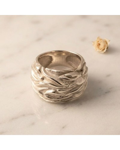 Alliance FLAMME pour femme en or: bague argentée texturée, motifs ondulés, plan marbre clair, petite rose pâle en arrière-plan