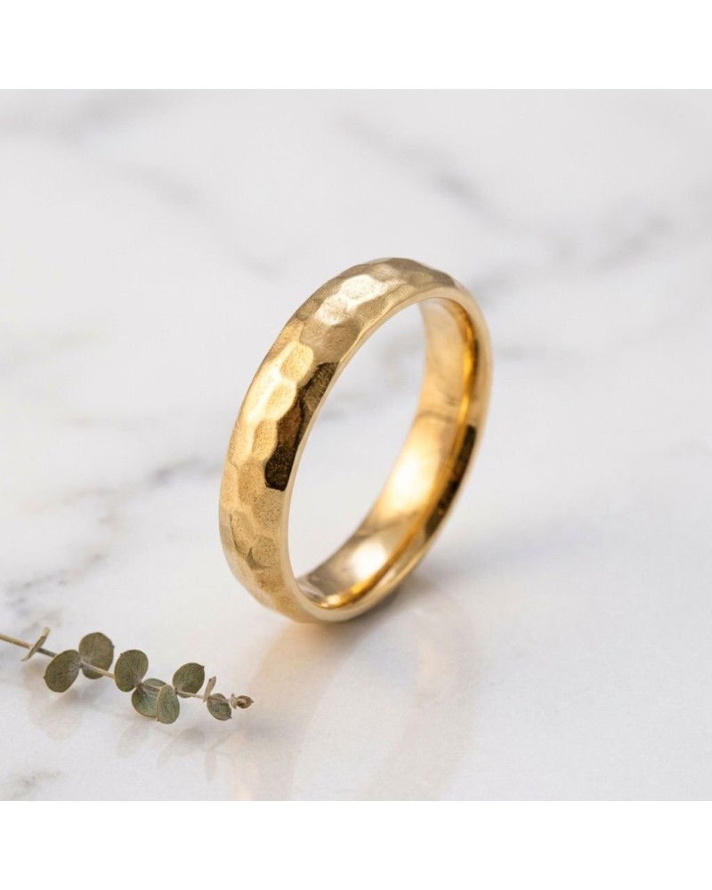 Alliance femme bombée martelée en or: bague artisanale sur mesure, détail texturé doré sur fond marbré.