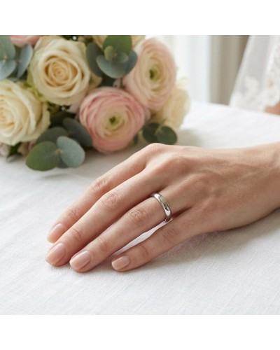 Alliance Basic Bombée femme en or : close-up d’une main feminine portant une bague simple et argentée, avec bouquet de roses pâl