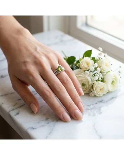 Alliance VENUS en or avec péridot, 6 tourmalines vertes et 16 diamants sur le doigt, bouquet blanc en arrière-plan.