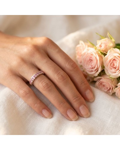 Alliance sertie par 9 saphirs roses synthétiques sur doigt féminin, avec bouquet de roses pastel en arrière-plan.