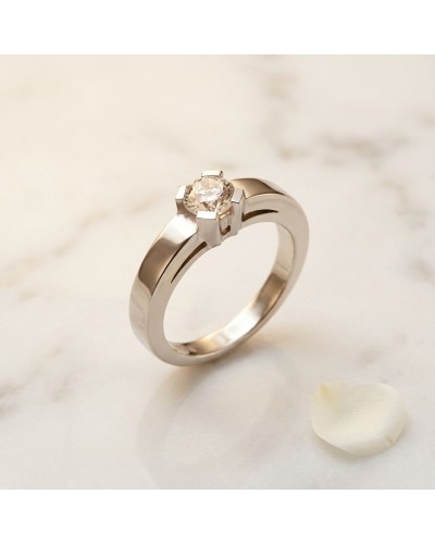Alliance HASRAT en or serti griffes avec diamant solitaire sur fond clair, pierre blanche près d'une pétale.