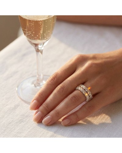 Alliance double rang en or sertie de 24 diamants sur le doigt, à côté d’un verre de champagne.
