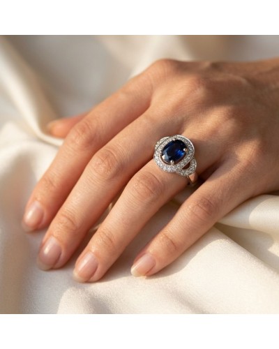 Alliance PROMESSE en or avec un large bijou serti de 29 diamants autour d’un saphir synthétique bleu profond posé sur le doigt.