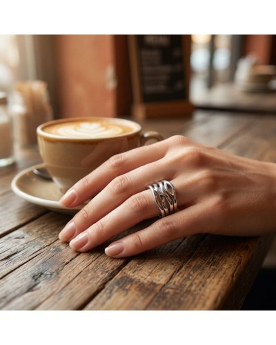 Alliance LITTLE ATiana en or: main féminine posée sur une table en bois près d’un café, portant une bague argentée design en fil