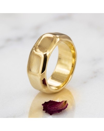 Alliance en écrou lisse pour femme en or, anneau doré plat, près d'une pétale violette.