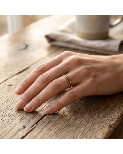Alliage fin incurvé pour femme: bague dorée portée sur le doigt, posé sur une table en bois.