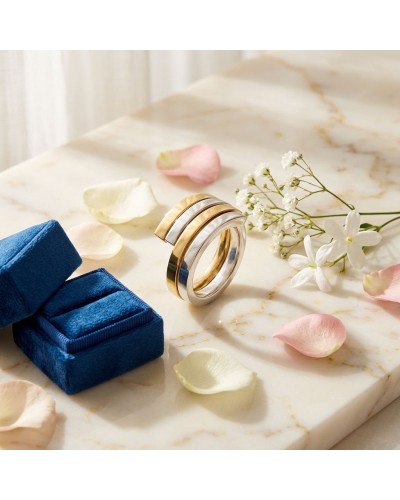 Alliance entrelacée bicolore femme en or : bague moderne dorée et argentée posée sur marbre, fleurs et pétales autour.