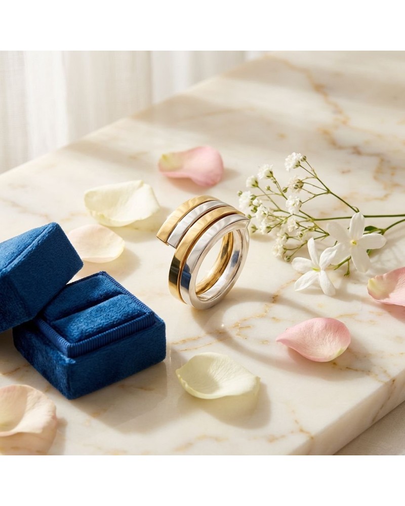 Alliance entrelacée bicolore femme en or : bague moderne dorée et argentée posée sur marbre, fleurs et pétales autour.
