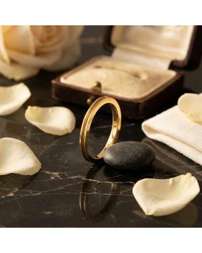 Alliance fine incurvée pour homme en or posée sur une pierre noire, avec boîte et pétales de rose autour.
