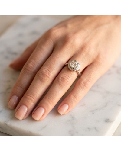 Bague SATURNE en argent avec pierre facettée sur doigt féminin posé sur une surface en marbre.