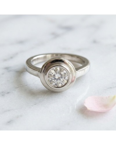 Bague Saturne en métal argenté avec pierre centrale scintillante rondelle, sur marbre, pétales près. (Bague SATURNE)
