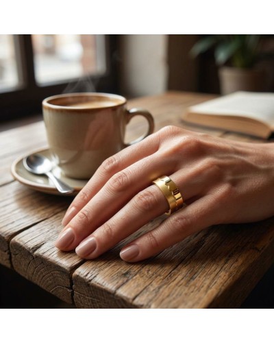 Alliance bi-matière femme en or sur doigt posé à côté d’une tasse de café.