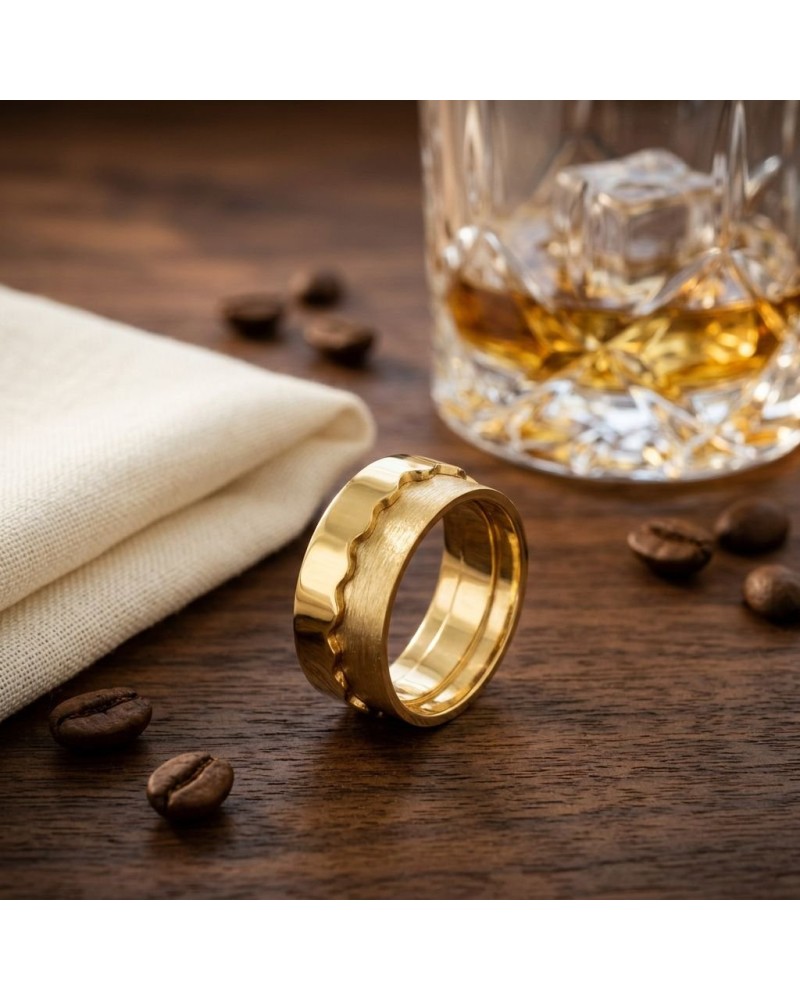 Alliance bi-matière homme en or: bague dorée avec bords ondulés, sur bois, près d’un verre de whisky et de grains de café.