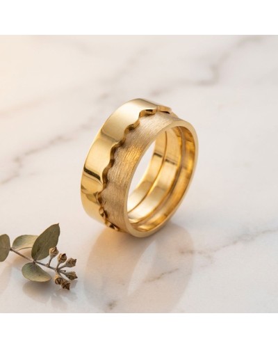 Alliance bi-matière homme en or: bague dorée à surface satinée avec arêtes irrégulières sur fond marbre, prêt pour homme.