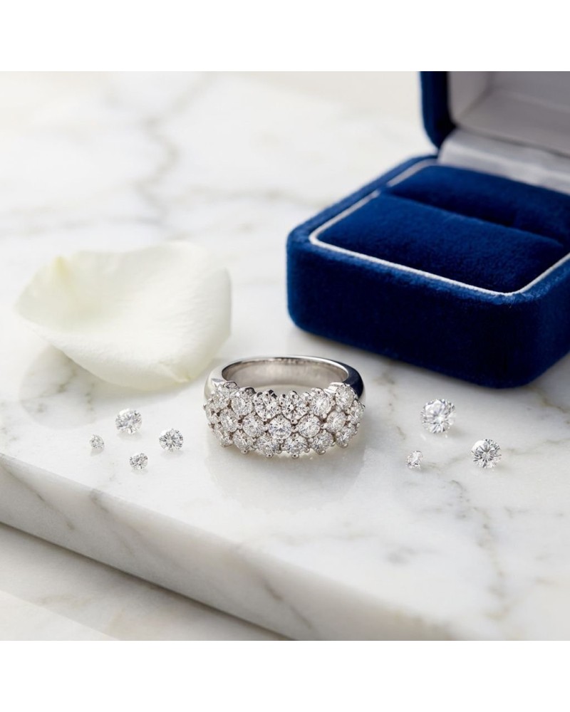 Alliance pavée sertie de 19 diamants avec entourage argenté, sur marbre près d’un boîtier bleu et pétales blancs.