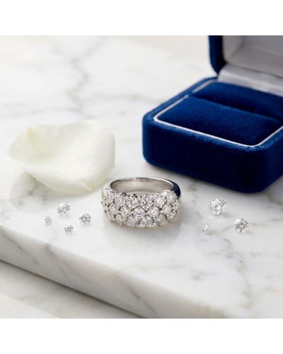 Alliance pavée sertie de 19 diamants avec entourage argenté, sur marbre près d’un boîtier bleu et pétales blancs.