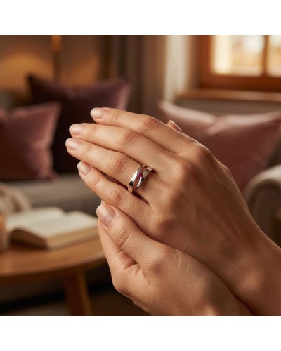 Alliance CROISADE en or avec rubis synthétique sur une main, fond intérieur chaleureux et bijoux visibles.