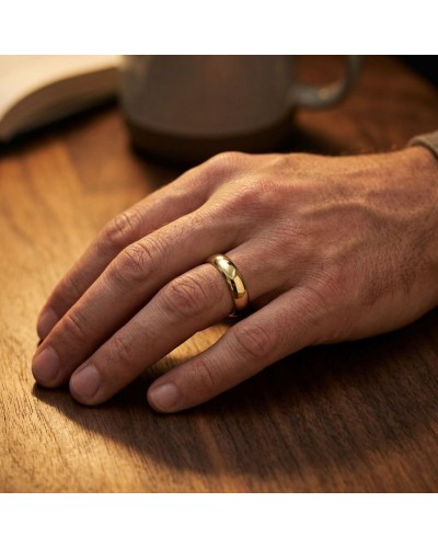 Alliance moyennement bombée pour homme en or, doigt posé sur table (close-up).