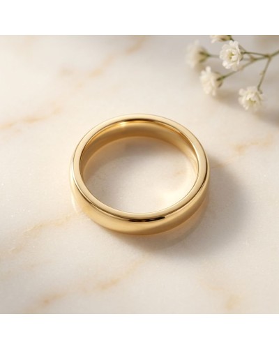 Alliance moyennement bombée femme en or: bague dorée lisse sur marbre, bouquet blanc en arrière-plan.