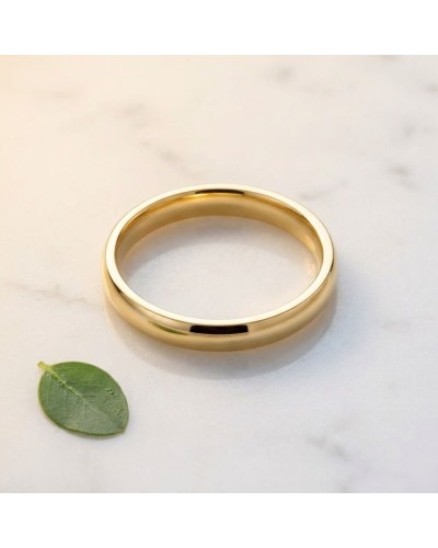 Alliance homme en or bombée, simple et lisse, posé sur marbre with small green leaf nearby.