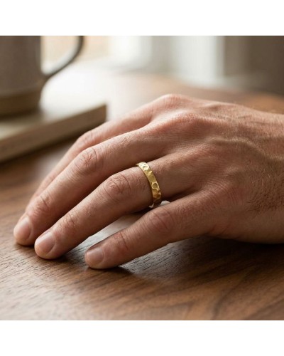 Alliance irrégulière martelée en or sur un doigt, image proche d’une main masculine sur une table en bois.