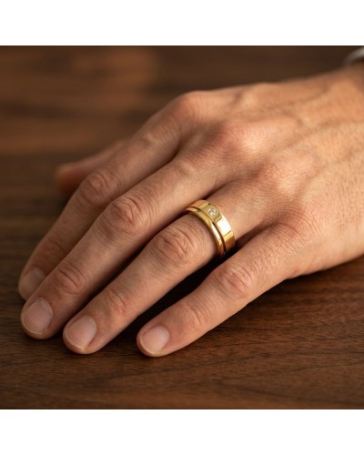 Alliance homme en or sertie d'un diamant, prise de vue rapprochée sur doigt posé sur bois.
