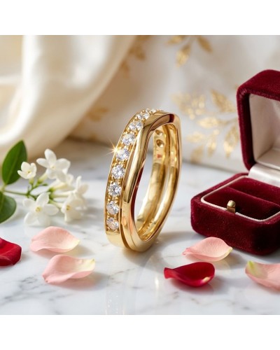 Alliance vague sertie de 13 diamants en or jaune, près d’une bague et d’un boîtier rouge, sur marbre avec pétales.