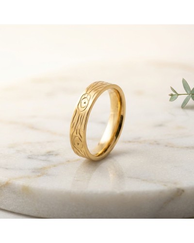 Alliance effet bois homme en or – bague dorée avec motif gravé sur marbre, proche d’une plante.