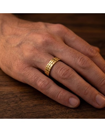 Alliance homme en or demi-effet crocodile, bague dorée portée sur doigt sur table en bois.