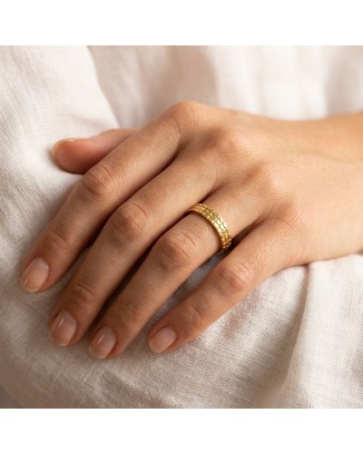 Alliance demi-effet CROCO femme en or portée sur le doigt, près d'une manche en tissu blanc.