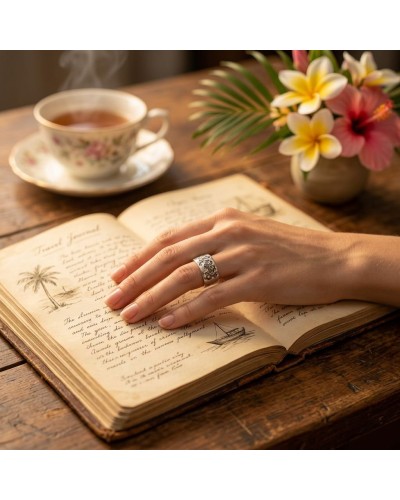 Bague FLORES GRAVEE argentée portée sur une main posée sur un livre ancien ouvert, à côté d’une tasse de thé fumant et d’un bouq