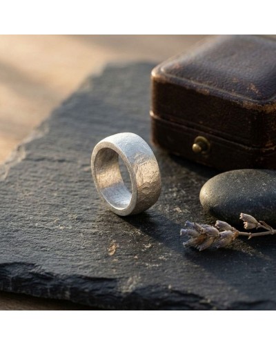 Bague ANNEAU en métal mat texturé, posée sur une pierre sombre avec une petite boîte vintage à l’arrière-plan.