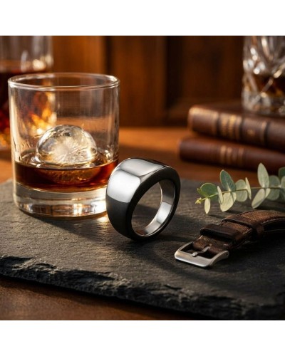 Bague BALI noire et argent posée sur une plaque sombre près d’un verre de whiskey et d’un bracelet en cuir, ambiance bar chic.