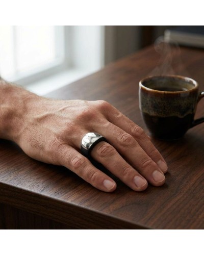 Anneau BALI en métal argenté brillant porté sur le doigt d’un homme, posé sur une table en bois près d’un café fumant.