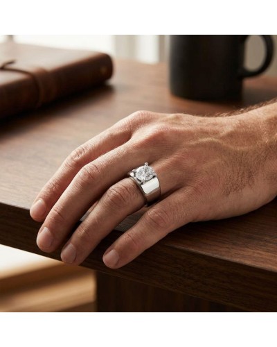 Bague PIKIRAN argentée à pierre centrale brillante portée sur l’annulaire droit d’une main masculine, sur table en bois avec liv