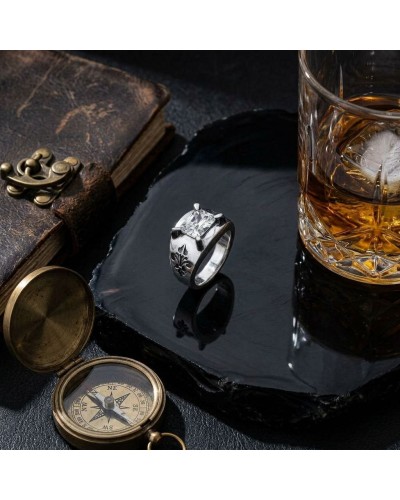 Bague MENTAWAÏ argentée avec motif fleur, posée sur une plaque noire près d’un verre de whiskey et d’un compas antique.