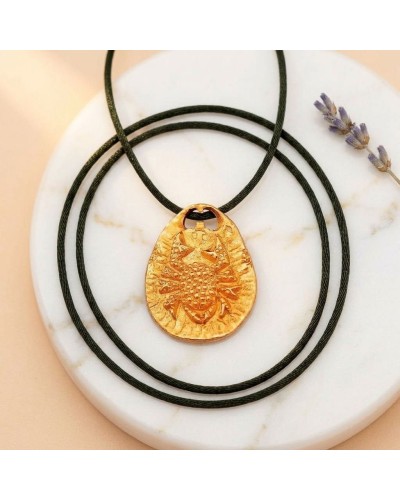 Pendentif zodiaque Cancer en or avec cordon noir et fermoir offert, posé sur disque en marbre.