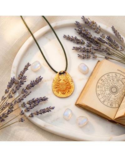 Pendentif zodiac Cancer doré avec cordon noir, fermoir offert, posé sur assiette en marbre avec fleurs de lavande et livre d’ast