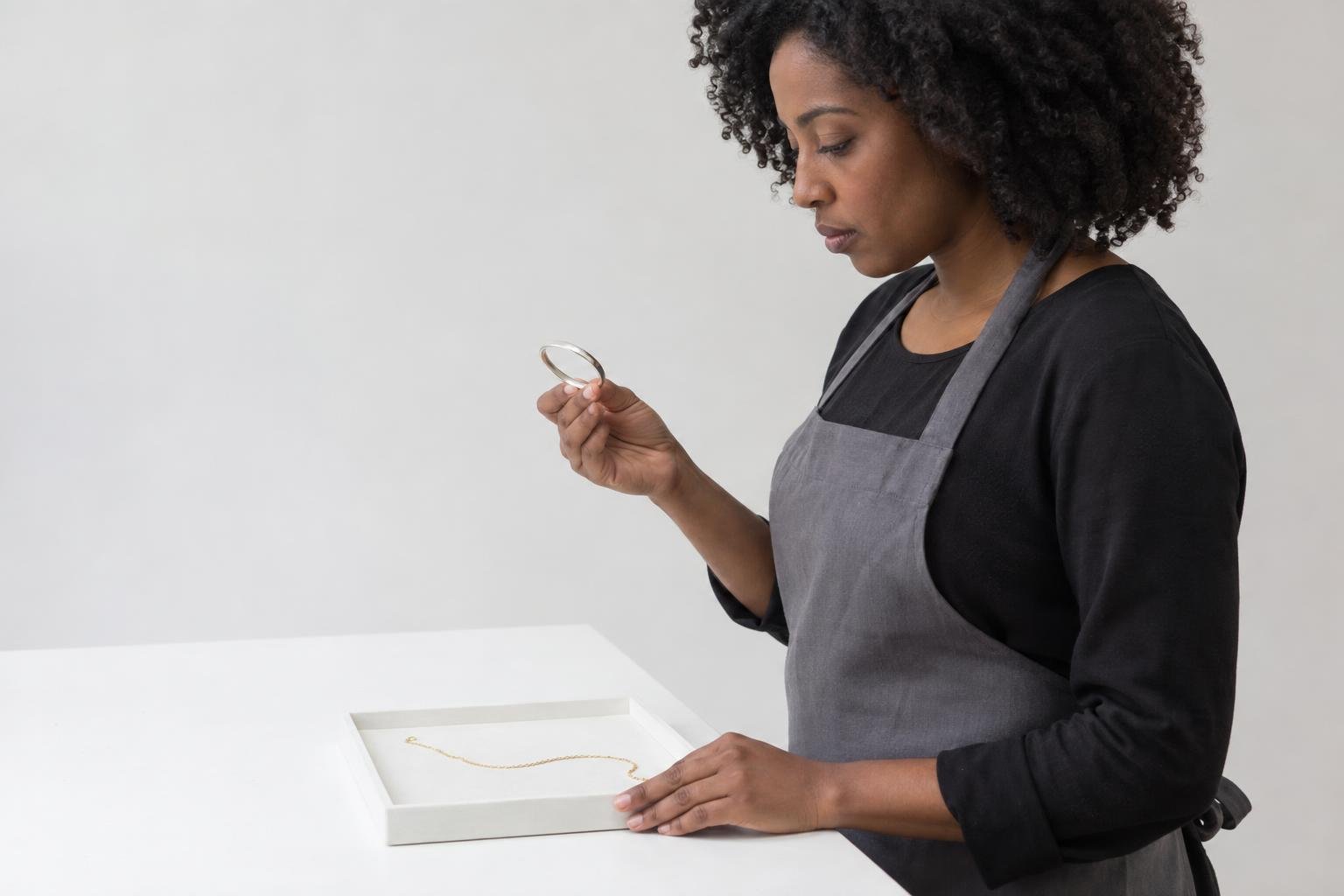 Une femme examine un bracelet posé dans un cadre sur une table.